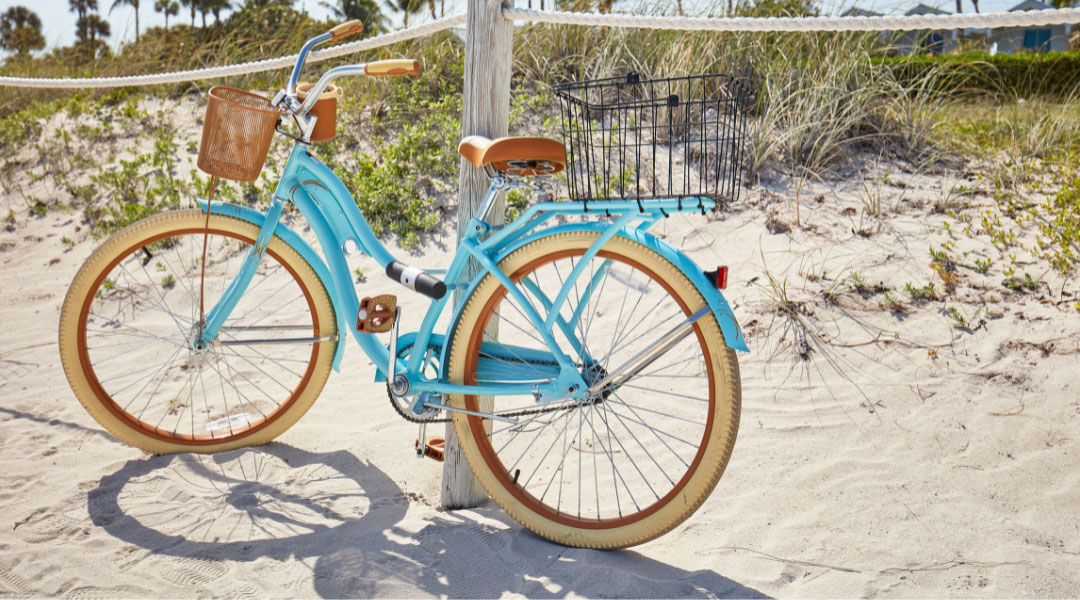 Blue bicycle with a basket in the front and back parked on the beach
