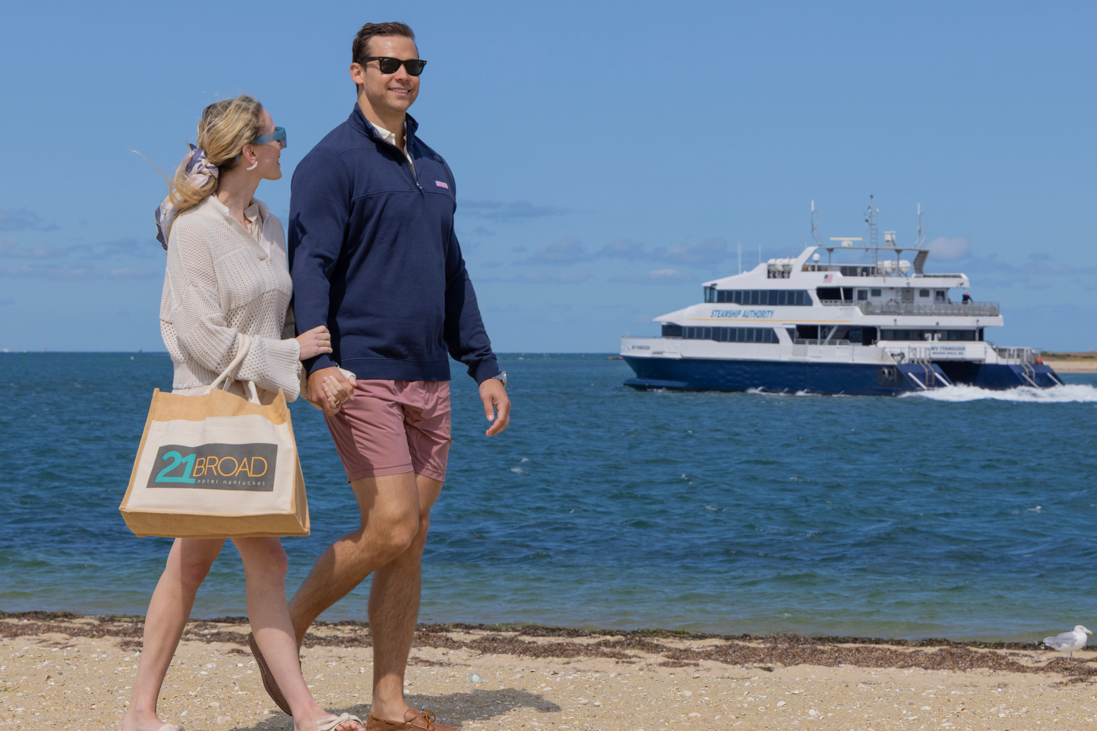 A Couple Walks Down The Beach In Nantucket With Ferry In The Background